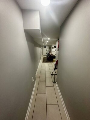 A narrow hallway with tiled flooring leading to a dining area with a table and chairs. - Cozy 2 BR Basement Suite (Washington)