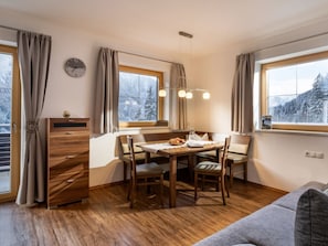 A cozy room with a wooden dining table, chairs, a sofa, and large windows with a view of snow-covered trees. - Heart of the Ahornblick House (Brandberg)