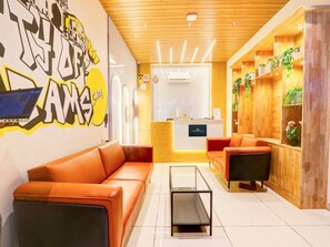 A modern lobby with a reception desk, orange seating, a glass coffee table, and a wall with a graphic design. - Townhouse Casa Grand Himayatnagar (Hyderabad)