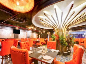 A restaurant interior with orange upholstered chairs, a central dining table, and a decorative ceiling feature. - Townhouse Casa Grand Himayatnagar (Hyderabad)