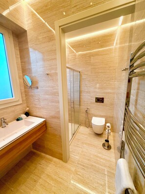 Un baño moderno con un espejo grande, un lavabo, un inodoro y una zona de ducha.
