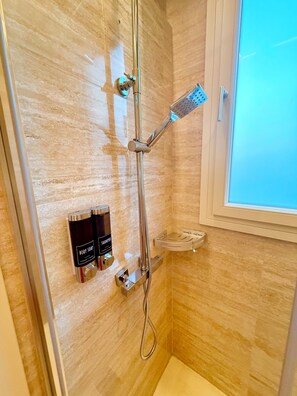 Un baño con ducha, una ventana y dos botellas de jabón de baño.