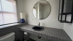 Un baño con inodoro, lavamanos, espejo y ventana con persianas.