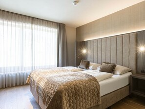 Ein Hotelzimmer mit einem großen Bett, einem Kopfteil mit integrierter Beleuchtung und einem Fenster mit transparenten Vorhängen.