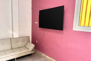 Quarto com sofá branco, parede rosa e televisão de tela plana preta fixada na parede.