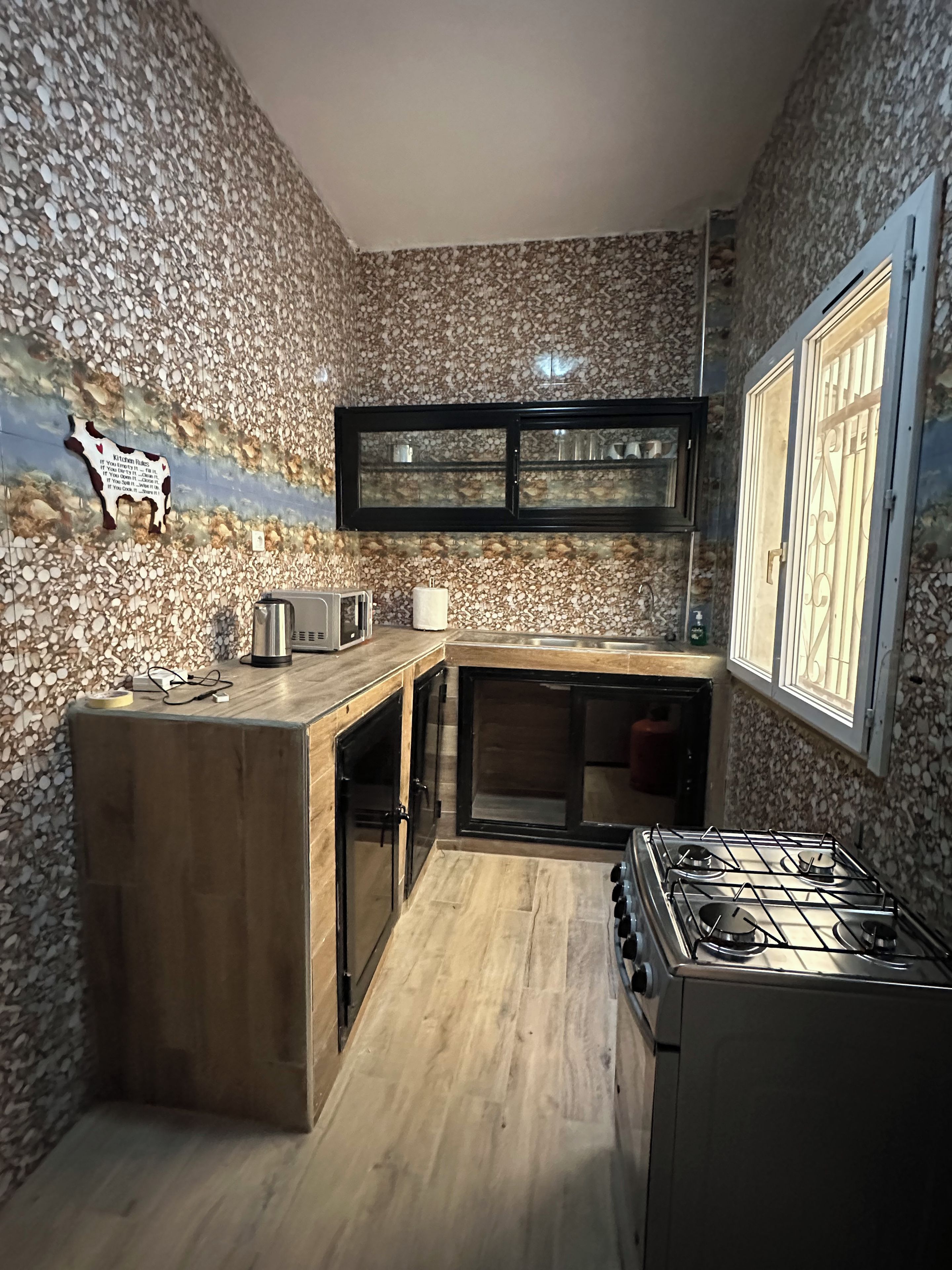 Cocina con salpicadero de pared de piedra, encimera de madera, estufa a gas y ventana con reja de metal.