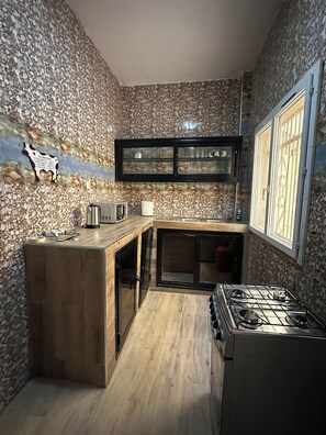 A kitchen with a stone wall backsplash, a wooden countertop, a gas stove, and a window with a metal grill. - Residences PRIM'IS Thies (Thies)