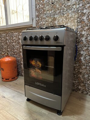 Cozinha com forno, botijão de gás e parede azulejada.