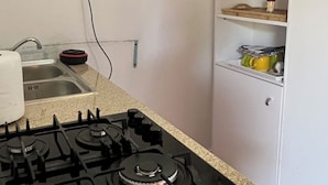 Cozinha com fogão a gás, pia e armário branco com prateleiras.