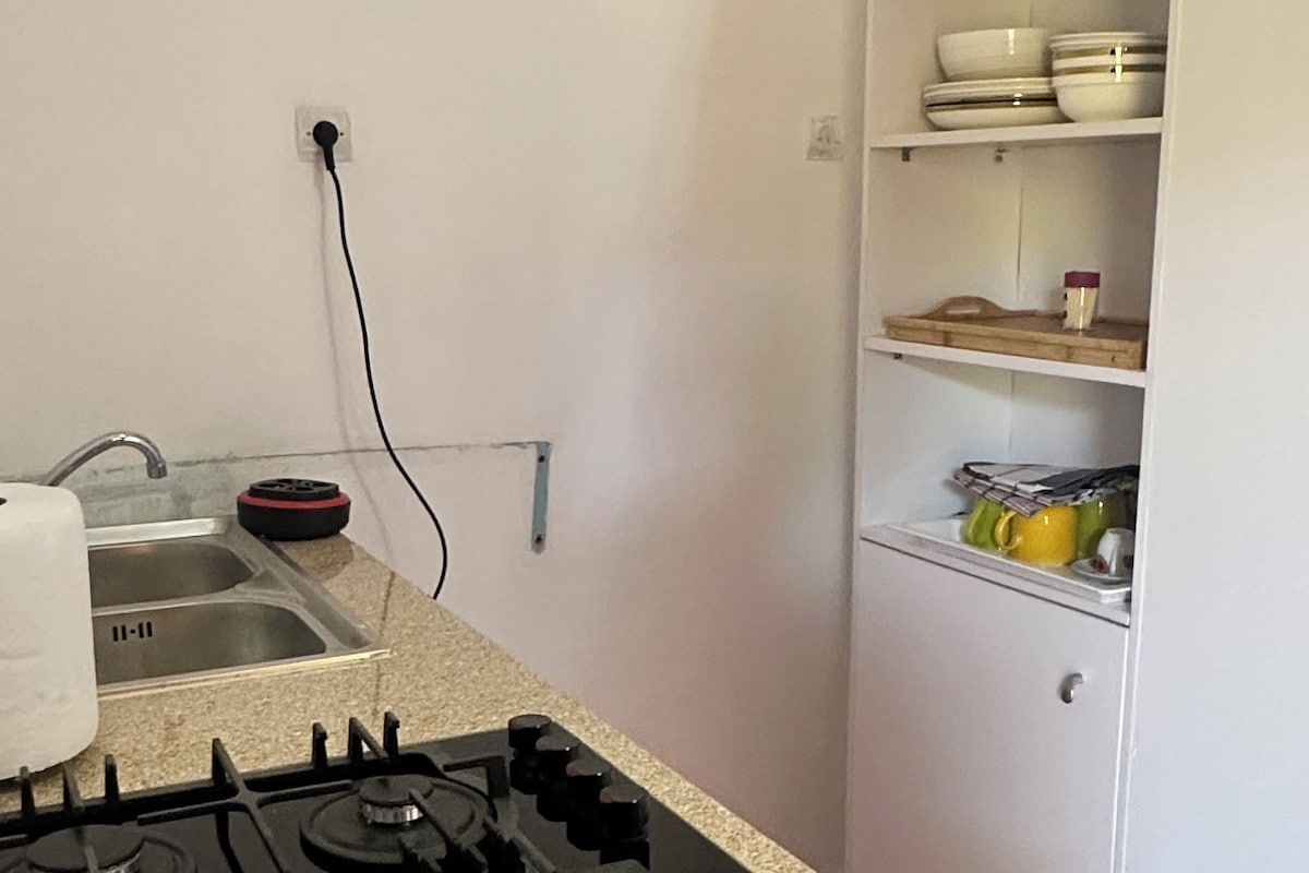 Une cuisine équipée d’une cuisinière à gaz, d’un évier et d’un meuble blanc avec des étagères.
