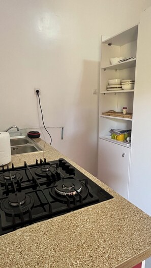 Une cuisine équipée d’une cuisinière à gaz, d’un évier et d’un meuble blanc avec des étagères.