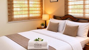 Cama bem arrumada com colcha branca e marrom, um travesseiro e uma toalha dobrada com um logotipo.