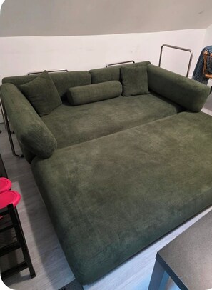 Un canapé vert avec des pieds en métal, une petite table avec un couvercle rouge et une chaise avec un dossier en tissu à mailles.