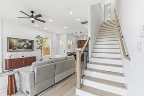 Ein modernes Wohnzimmer mit einem grauen Ecksofa, einer Holztreppe und einem Deckenventilator.