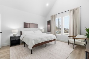A modern bedroom with a large bed, bedside lamps, a chair, and a view of the city through the window. - 3-bedroom house with AC in Houston neighborhood (Houston)