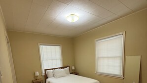 A bedroom with a bed, two bedside tables, a nightstand, and a window with blinds. - Waterbury Home (Des Moines)