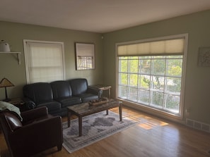 A living room with a sofa, a coffee table, a rug, and a large window with blinds. - Waterbury Home (Des Moines)