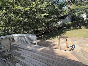 A wooden deck with a white railing, a bench, and a stone patio area. - Waterbury Home (Des Moines)