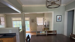A dining area with a dark wooden table and chairs, a kitchen area with wooden cabinets, and a view of the outdoors through large windows. - Waterbury Home (Des Moines)