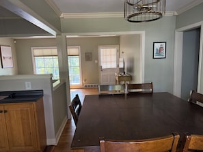 Un comedor con mesa y sillas de madera oscura, una zona de cocina con armarios de madera, y vistas al exterior a través de amplios ventanales.