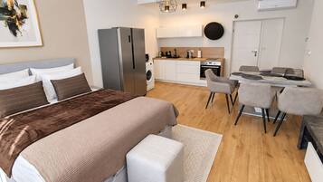 Un dormitorio moderno con una cama grande, una sala de estar separada con una mesa y sillas, lavadora incorporada y kitchenette.