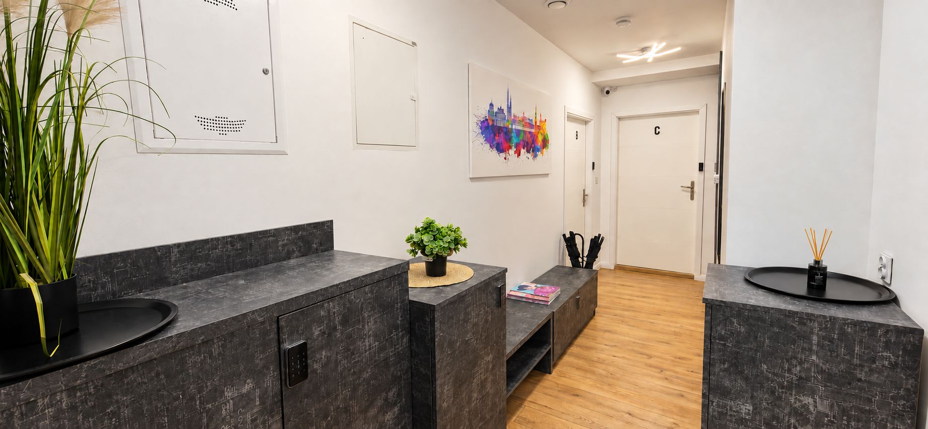 Un moderno vestíbulo de hotel con mostradores de mármol oscuro, una planta en maceta, una obra de arte urbana y colorida, y piso de madera.