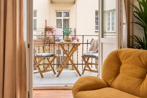 Una habitación con vista a un balcón, una mesa con sillas y una planta.
