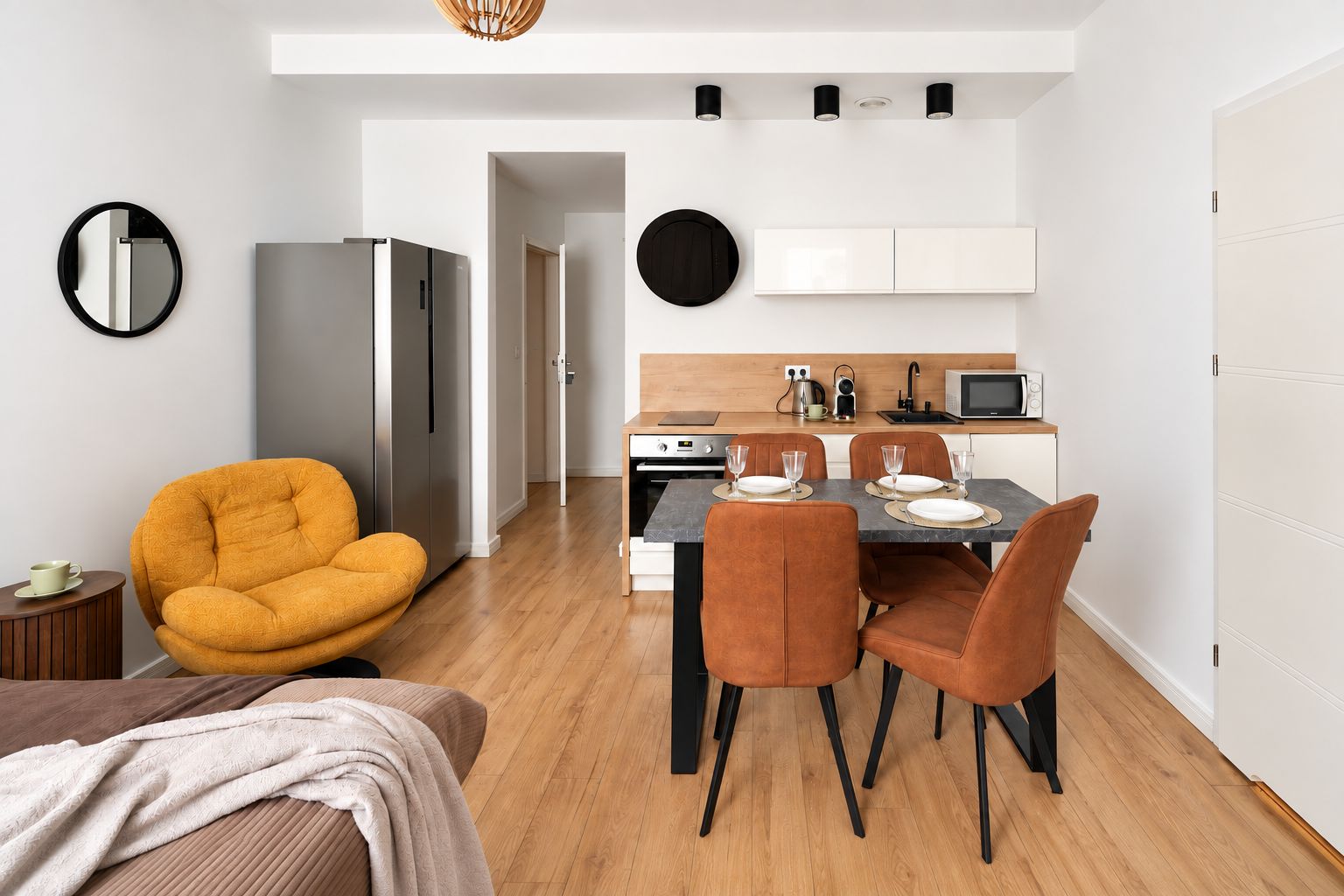 Una cocina moderna con armarios blancos, una mesa de comedor para cuatro personas y un refrigerador compacto.