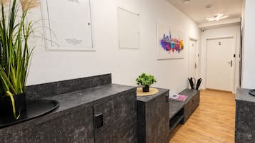 Un moderno vestíbulo de hotel con mostradores de mármol oscuro, una planta en maceta, una obra de arte urbana y colorida, y piso de madera.