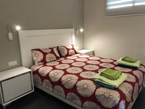 A neatly made bed with a patterned bedspread, two pillows, and folded towels on the side. - Ocean Breeze Apartment on El Duque Beach (Costa Adeje)