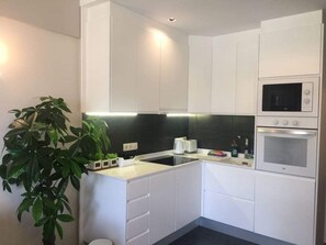 A modern kitchen with white cabinetry, a black backsplash, a microwave, and an oven. There is a plant on the counter. - Ocean Breeze Apartment on El Duque Beach (Costa Adeje)