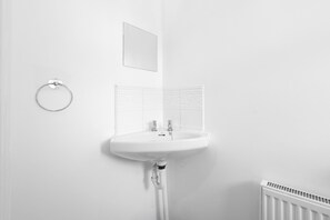 A white bathroom with a pedestal sink, a towel ring, a mirror, and a radiator. - 4-Bed Townhouse in Hamilton with Parking (Leicester)