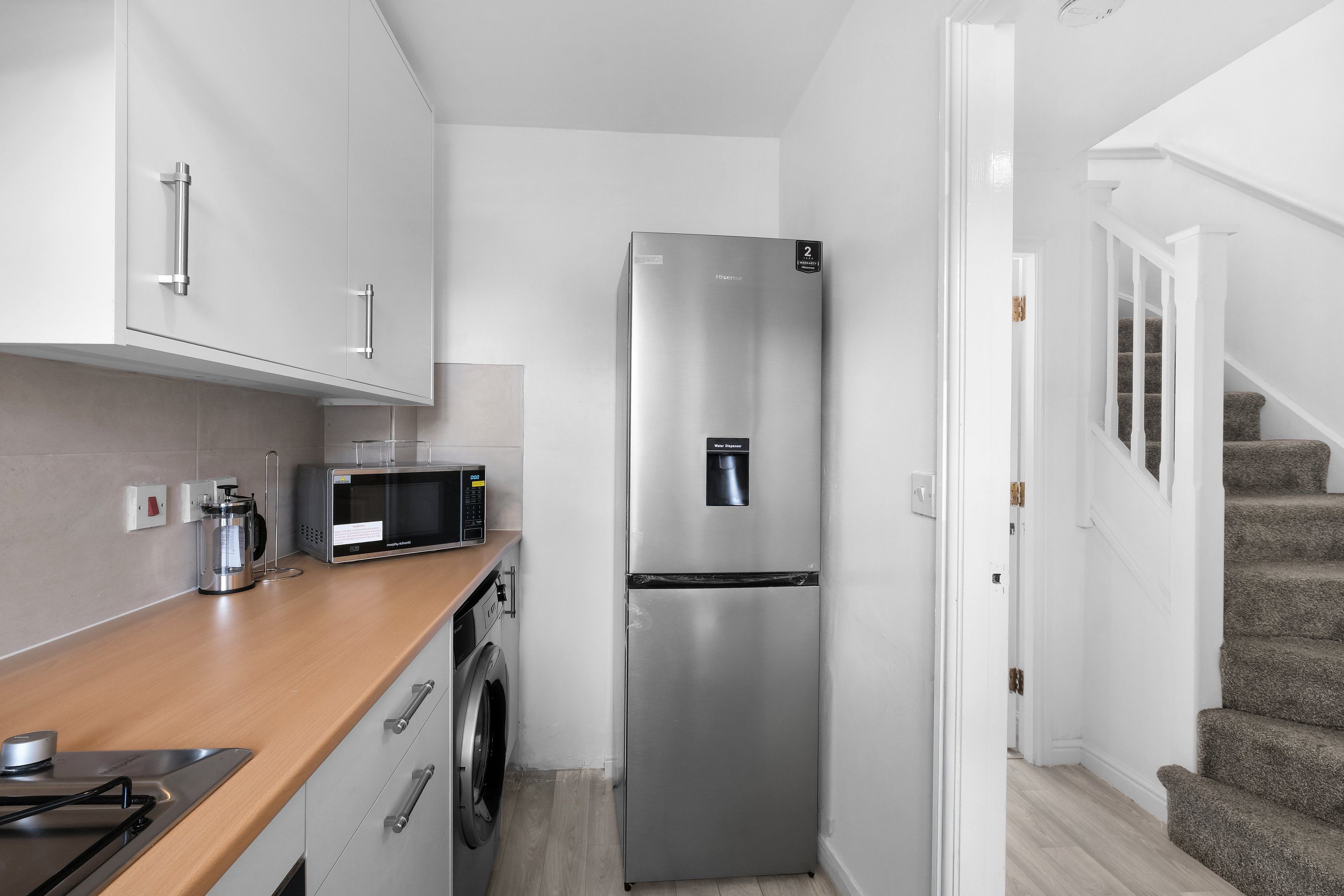 A compact kitchen with a stainless steel refrigerator, a microwave, and a washing machine.