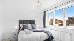 Ein Schlafzimmer mit Bett, Nachttischen, einem Fenster mit Blick auf Häuser und einer Chandelier.