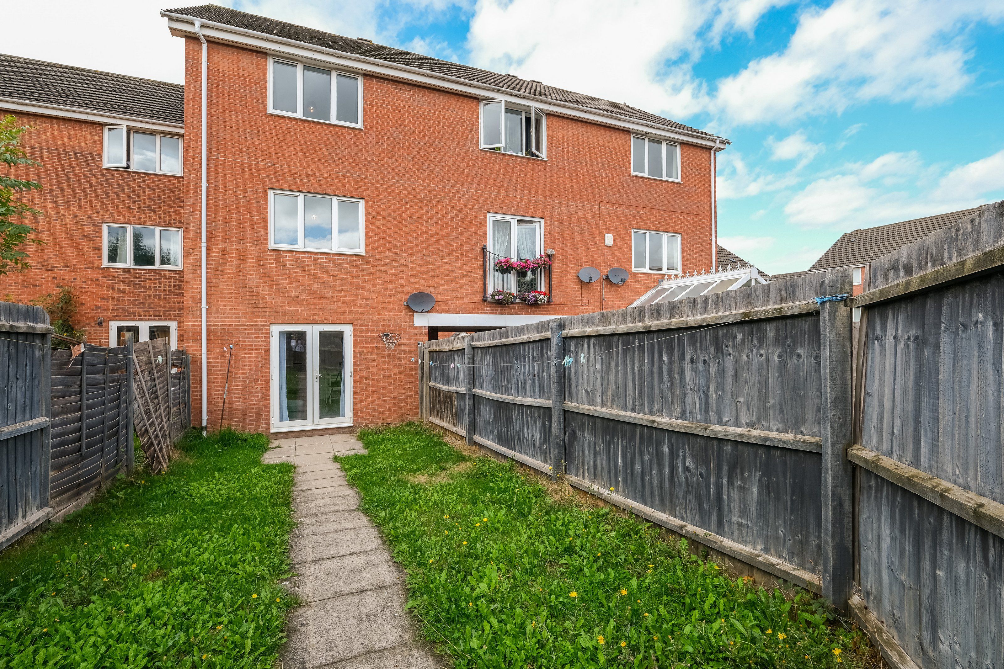 A brick apartment with a wooden fence, a pathway, and a door leading to a garage.