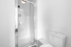 A modern bathroom with a glass shower enclosure, a toilet, and a showerhead. - 4-Bed Townhouse in Hamilton with Parking (Leicester)