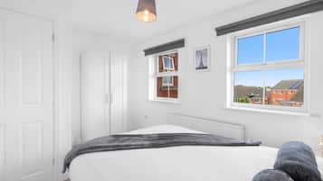 Ein Schlafzimmer mit einem Bett, einem Fenster mit Blick auf Gebäude und einer Deckenleuchte.