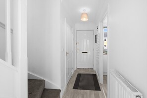A narrow hallway with a door at the end, a radiator on the right, and a light fixture above. - 4-Bed Townhouse in Hamilton with Parking (Leicester)