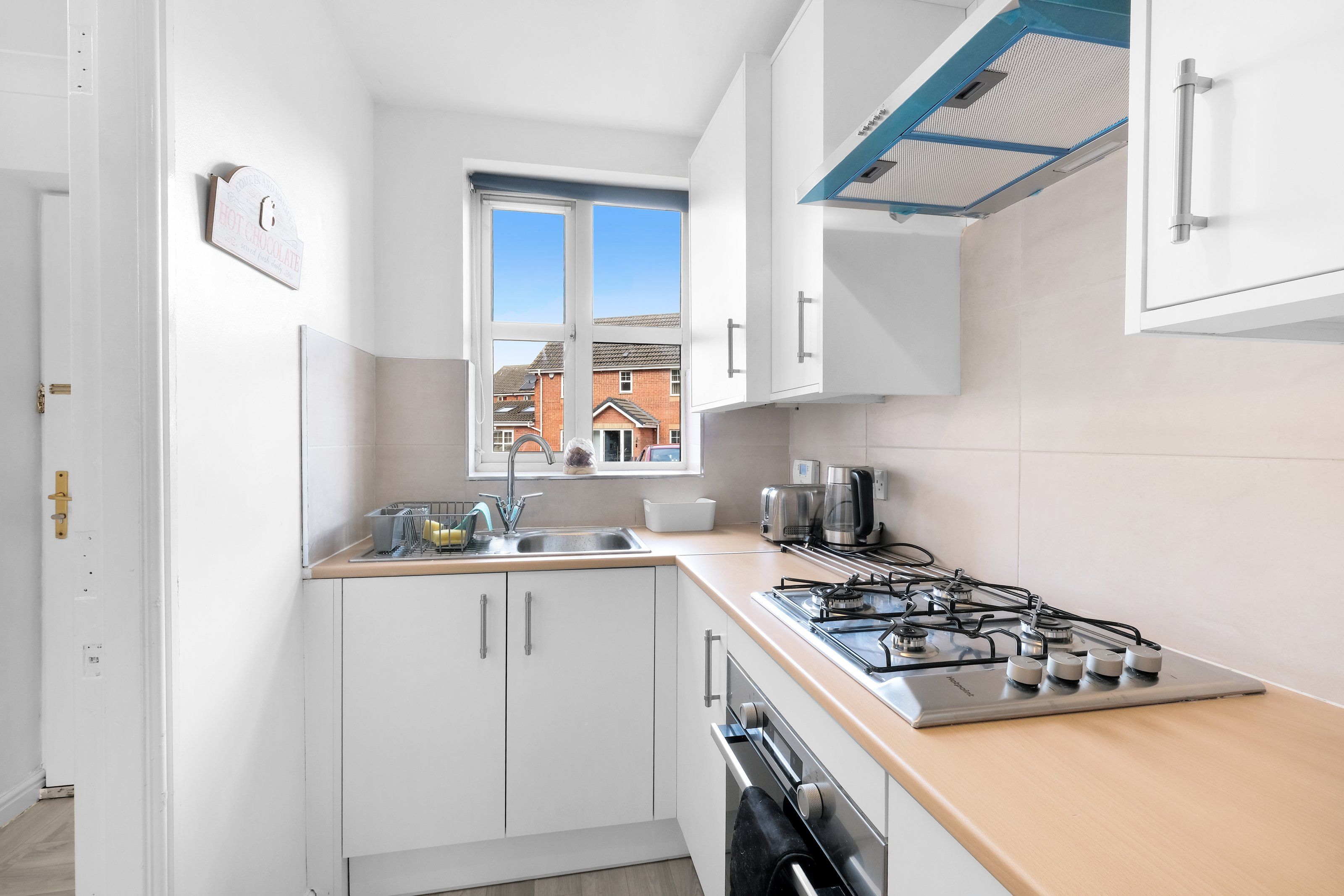 A compact kitchen with white cabinets, a gas stove, a sink, and a window overlooking a residential area.