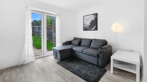 Ein modernes Wohnzimmer mit einem grauen Ecksofa, einem weißen Beistelltisch, einem schwarzen Teppich, einem gerahmten Kunstwerk und einer Stehlampe.