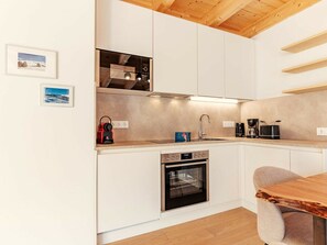 A modern kitchen with white cabinetry, a built-in oven, a sink, and a wooden dining table. - Cabin in Niederwolz With Sauna (Oberwölz)