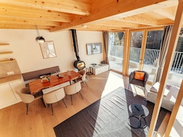 En modern inredning med ett träpanelat tak, en matplats med bord och stolar, en soffa, en öppen spis och en balkong med utsikt.