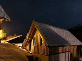 Una cabaña de madera con techo inclinado, una ventana visible y suelo cubierto de nieve.