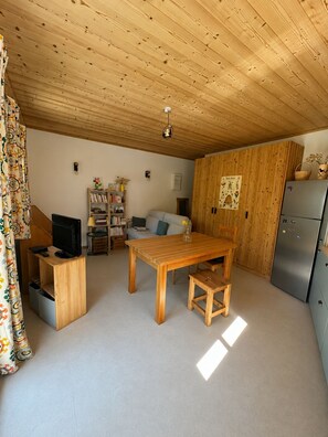 A cozy room with a wooden ceiling, a dining table, a sofa, a bookshelf, a television, and a refrigerator. - New Condo / Sleeps 4 / Right on the slopes - Les Menuires (Les Belleville)