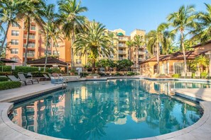 A swimming pool surrounded by palm trees and a multi-story building with balconies. - Aventura Eden - 2-bedroom, Pool, Gym, Mall and Beach Oasis (Miami)