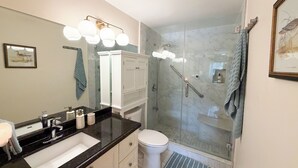 Ein modernes Badezimmer mit einer gläsernen Duschkabine, einer weißen Toilette und einem schwarzen Waschtisch.