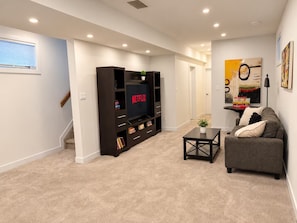A living room with a flat-screen TV, dark wooden entertainment unit, a gray sofa, and a small coffee table. - Central Edmonton Home | Walk to 124St Restaurants | 5min downtown | Pet Friendly (Edmonton)