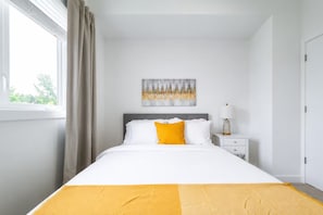 A hotel room with a bed, a nightstand, a lamp, and a window with curtains. - Central Edmonton Home | Walk to 124St Restaurants | 5min downtown | Pet Friendly (Edmonton)