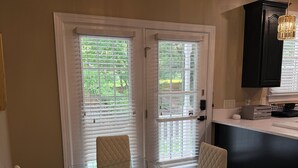 A dining area with a glass table and four chairs, a kitchen with dark cabinetry, and a pendant light. - Serene 4-bedroom house near Elon (Burlington)