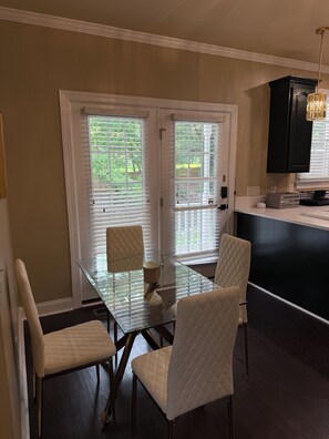 Un comedor con una mesa de vidrio y cuatro sillas, una cocina con muebles oscuros y una lámpara colgante.